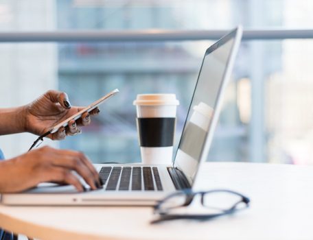 Image of person flexible working on laptop on table with coffee and glasses