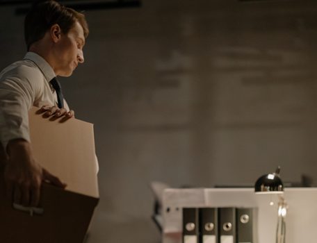 white man holding cardboard box staring at desk following unfair dismissal