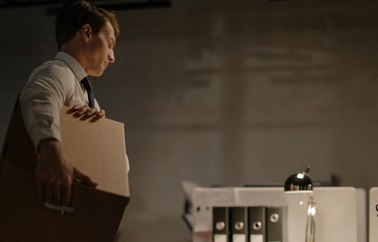 white man holding cardboard box staring at desk following unfair dismissal