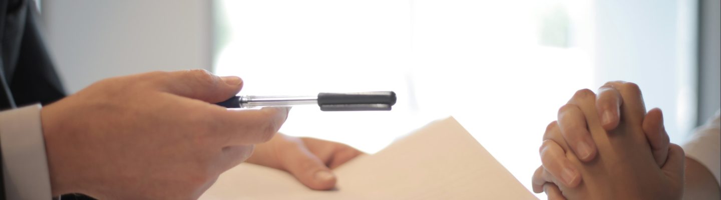 Image of two people sitting at a table signing a piece of paper for a Settlement Agreement