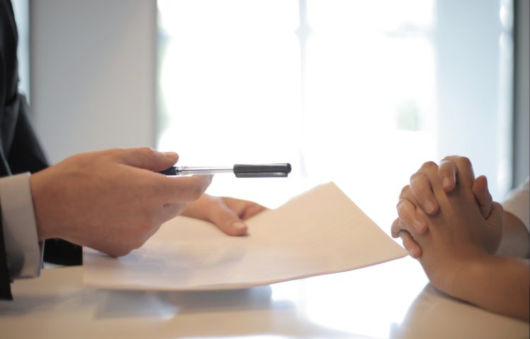 Image of two people sitting at a table signing a piece of paper for a Settlement Agreement