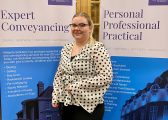 Picture of Abigail Morrison a white woman with blonde hair wearing a patterned top standing in front of two Hibberts Solicitors Pull up Banners