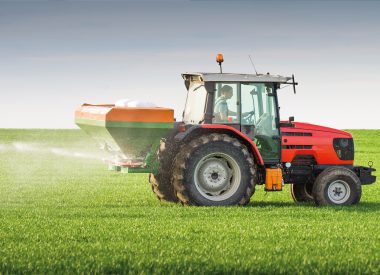 Image of a red tractor on a spraying a green field for the Inheritance Tax Blog
