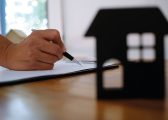 Image of a hand holding a pen and a cardboard cutout of the front of a house sitting on a desk for the Renters Rights Bill