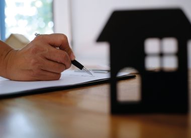 Image of a hand holding a pen and a cardboard cutout of the front of a house sitting on a desk for the Renters Rights Bill