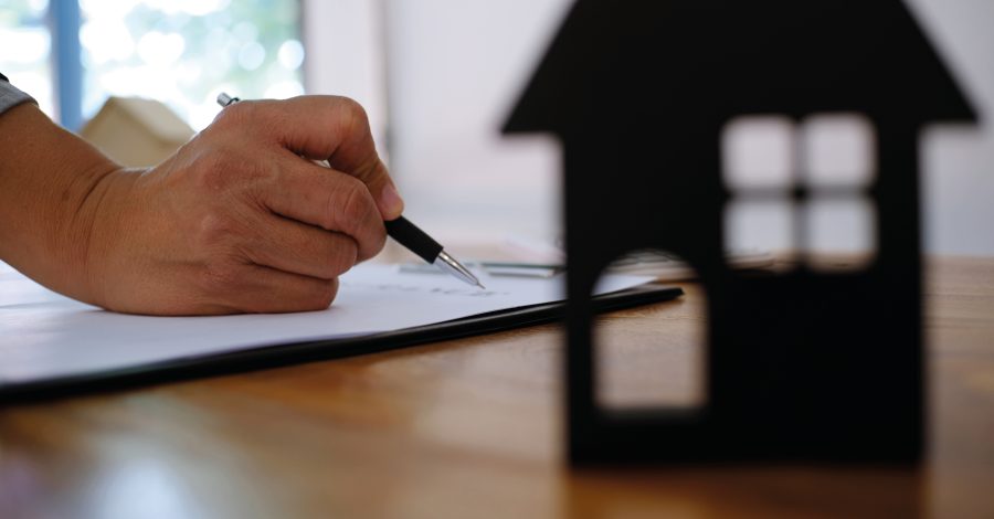 Image of a hand holding a pen and a cardboard cutout of the front of a house sitting on a desk for the Renters Rights Bill